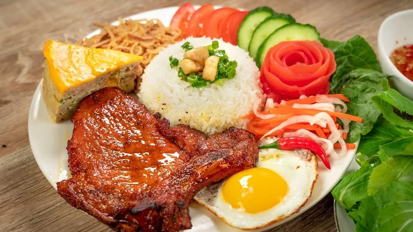 Broken rice topped with a juicy grilled pork chop, savory egg meatloaf (chả chưng), and crispy shredded pork skin (bì). This is breakfast, lunch, and dinner perfection.